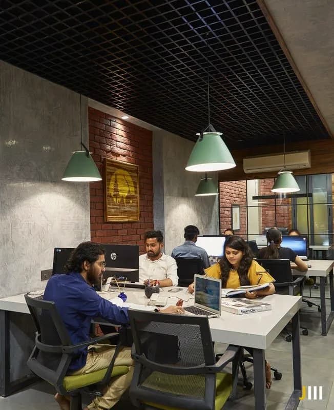 A team at shared desks under pendant lights and an open grid ceiling.