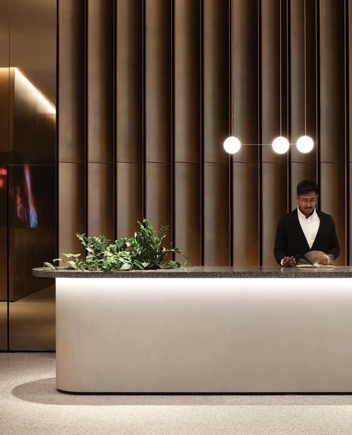 Reception counter lit from below, fluted wall and three pendant globes.