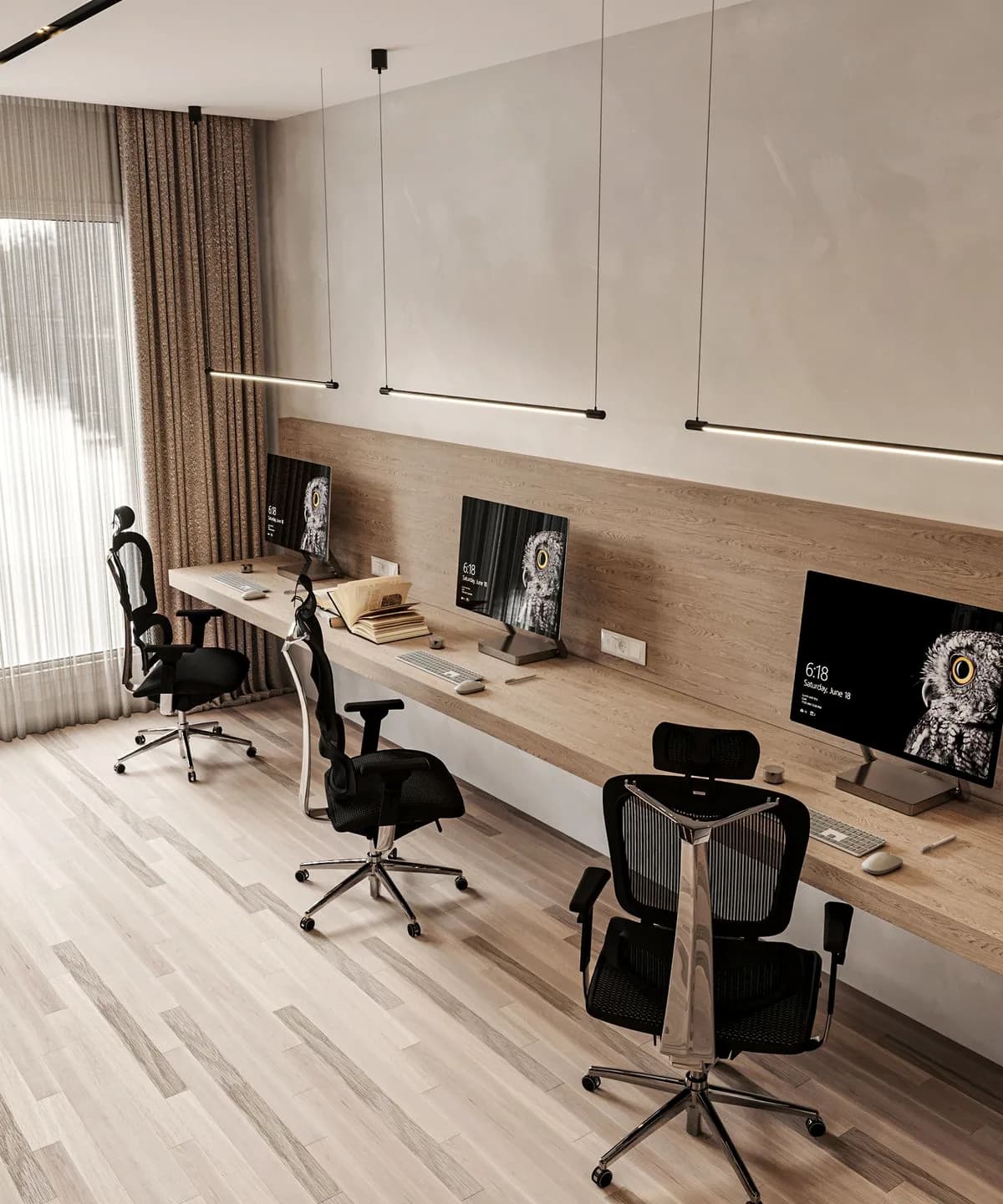 A long shared desk under pendant lines, three screens, a curtained window.