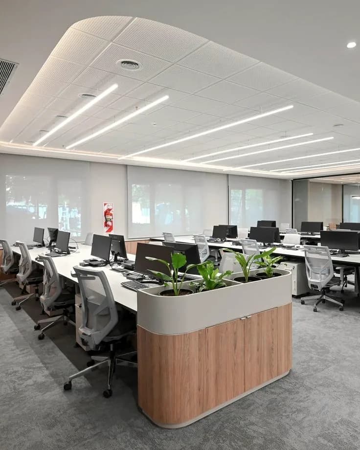 Workstations in rows beneath a grid ceiling, glazing along one wall.